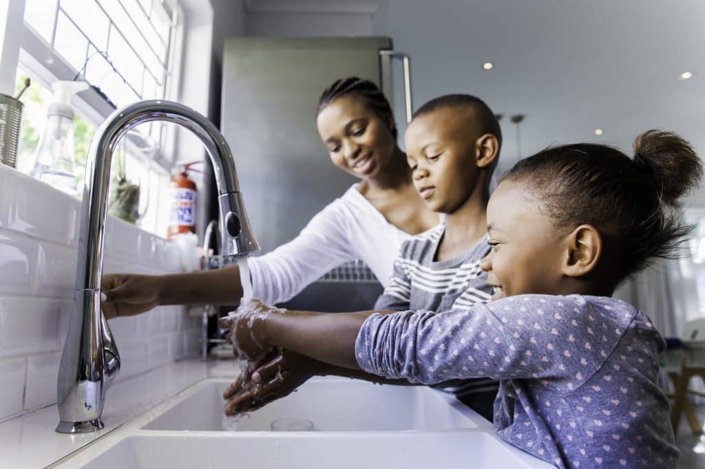 A mother turns on the faucet for her son and daughter to wash their hands.