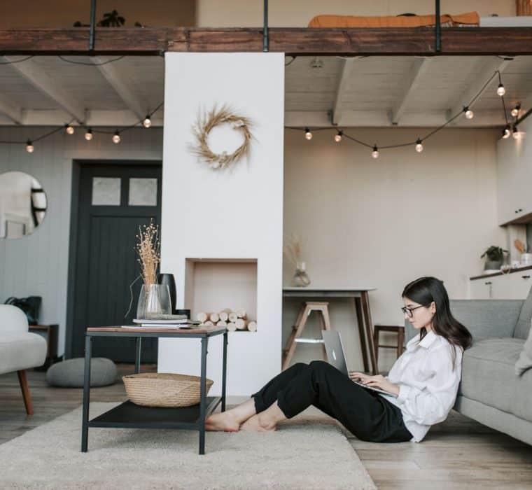 A woman sits on her floor at home on her laptop scrolling through social media and emails - during quarantine, it is a great time to do email marketing.