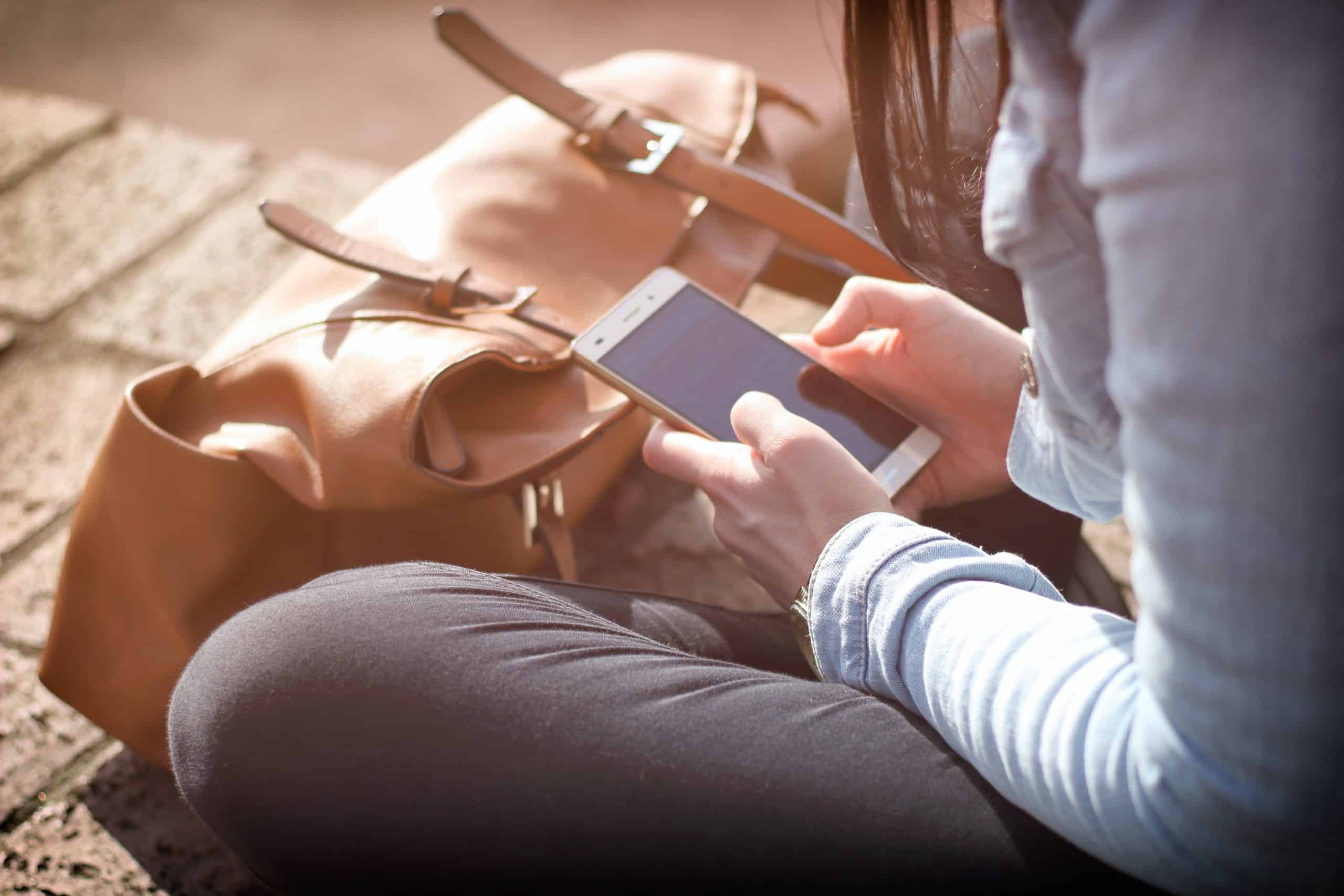 A woman fills out a mobile form while sitting in the sun on her lunch break.