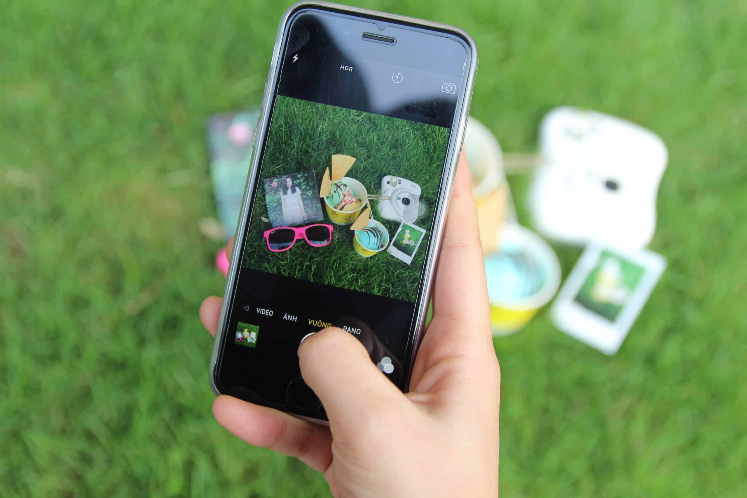 A user taking a photo of an assortment of products against a grassy background.