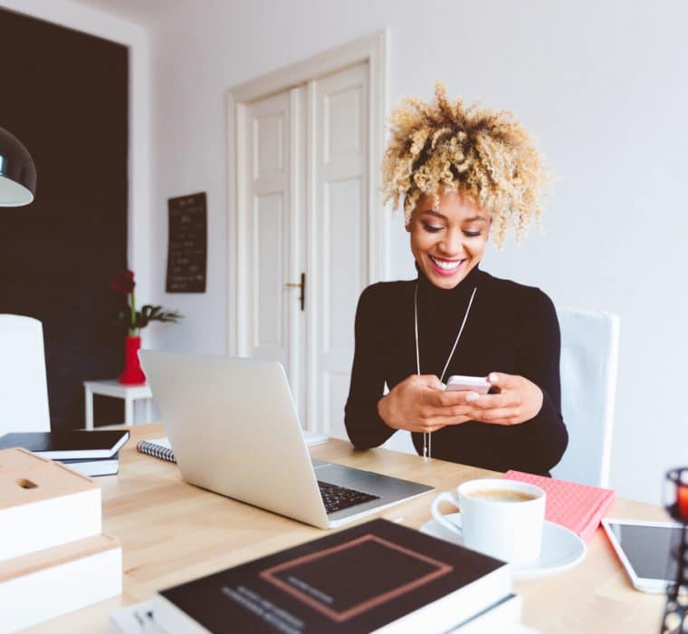 Marketer sits at her desk looking at her phone and learning about social media trends.