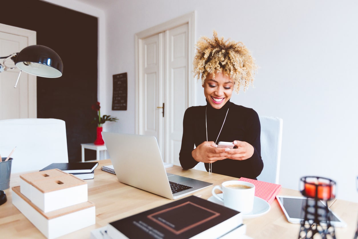 Marketer sits at her desk looking at her phone and learning about social media trends.