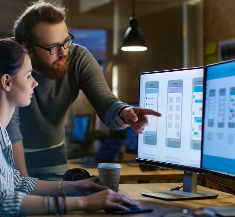 Man and woman looking at computer screen with mobile app design drafts on the screen