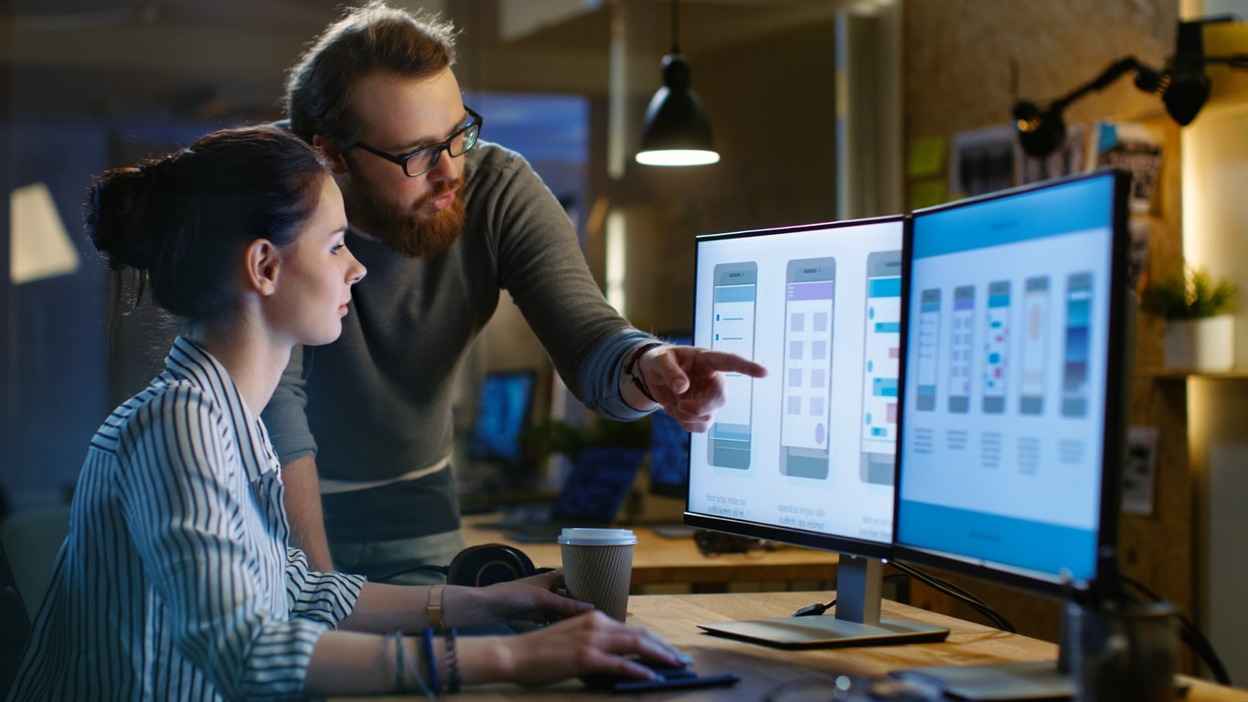 Man and woman looking at computer screen with mobile app design drafts on the screen