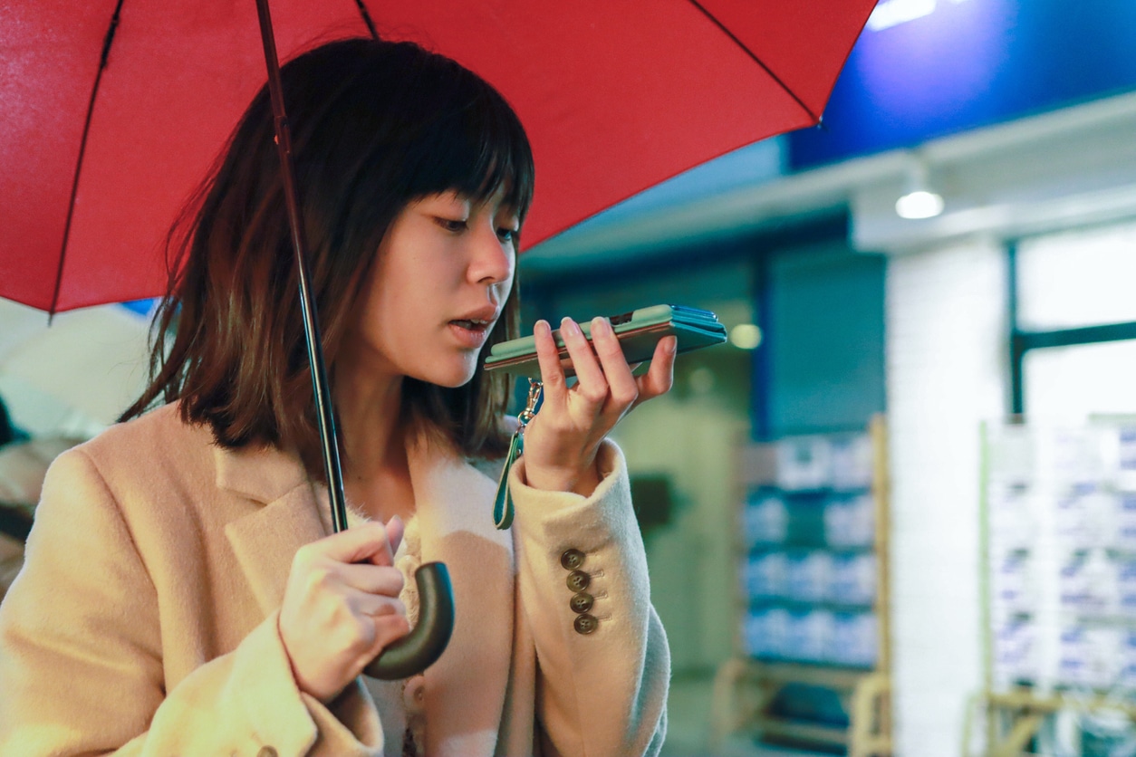 Women under red umbrella using her phone for voice search in city.