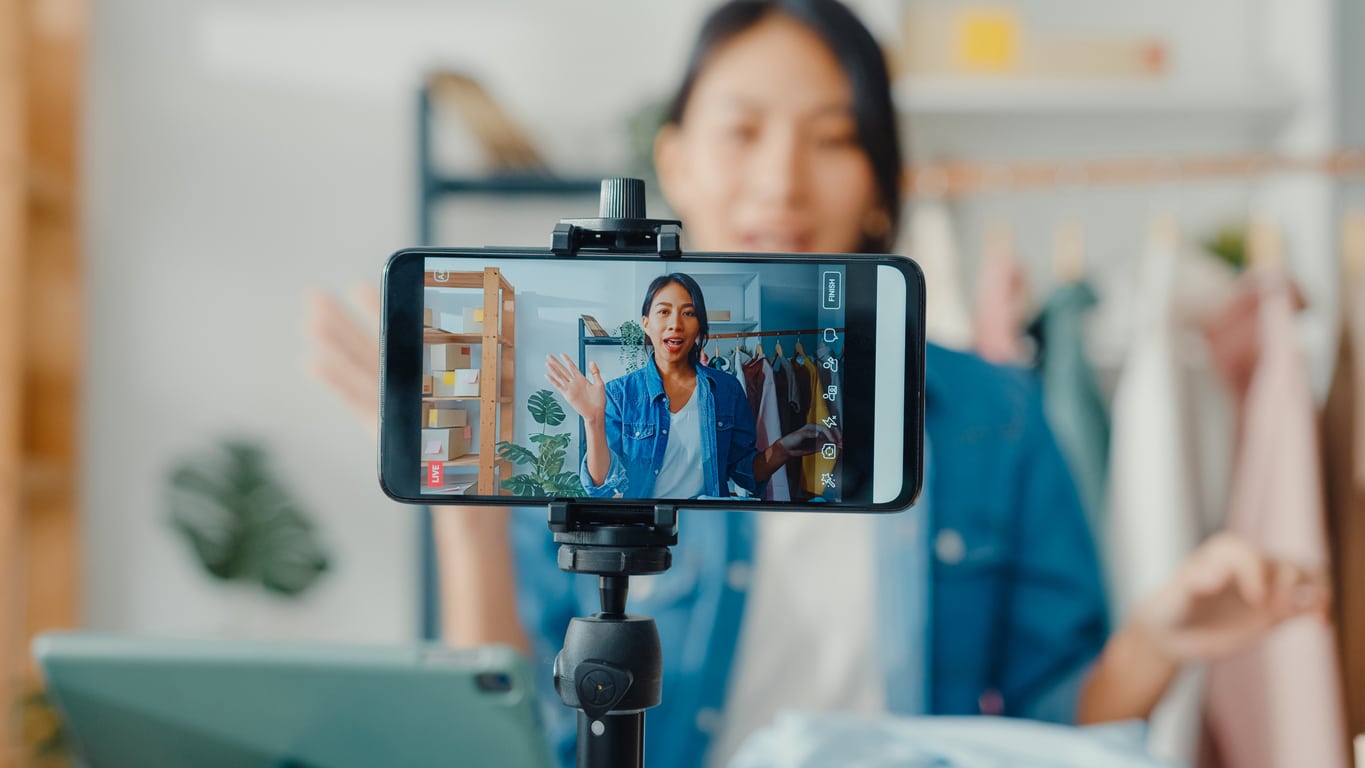 A smart phone in a stand recording a lady talking about her fashion business in her new video marketing strategy.